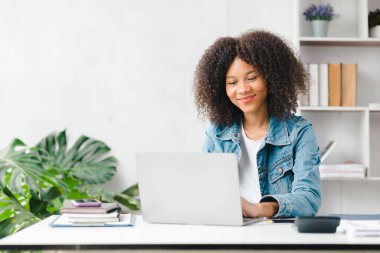 American teenage woman sitting in white office with laptop, she is a student studying online with laptop at home, university student studying online, online web education concept.