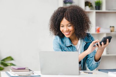 American teenage woman presses calculator against laptop, she is a student studying online with laptop at home, university student studying online, online web education concept.