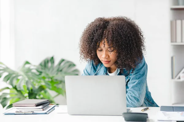 American teenage woman sitting in white office with laptop, she is a student studying online with laptop at home, university student studying online, online web education concept.