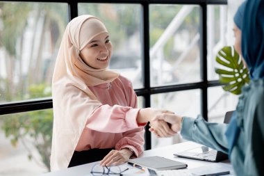 Two hijab Asian women shaking hands after a startup company meeting. run by a young, talented woman. The management concept runs the company of female leaders to grow the company.