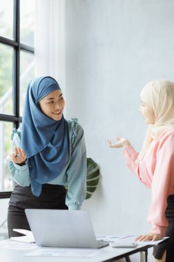 Two hijab-clad Asian women are brainstorming together in a conference room for a startup, run by a young, talented woman. The management concept runs the company of female leaders to grow the company.
