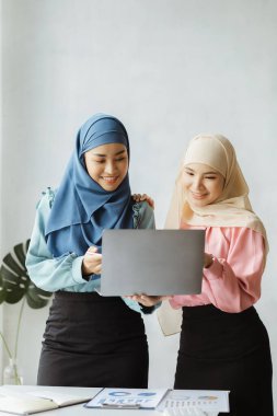 Two hijab-clad Asian women are brainstorming together in a conference room for a startup, run by a young, talented woman. The management concept runs the company of female leaders to grow the company.