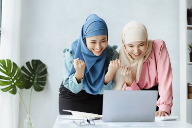 Two hijab Asian women look at growing company operating data on laptops and show joy. run by a young, talented woman. The management concept runs the company of female leaders to grow the company.
