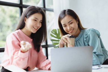 Girişim şirketinin atmosferinde, iki kadın çalışan, satışları artırmak ve yöneticilere raporlar hazırlamak için özetler ve pazarlama planları üzerinde çalışmak üzere fikir alışverişinde bulunuyorlar..