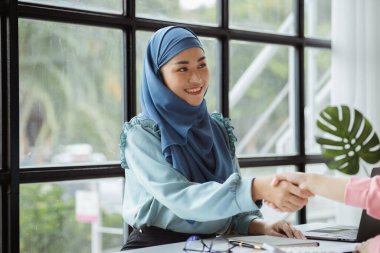 Two hijab Asian women shaking hands after a startup company meeting. run by a young, talented woman. The management concept runs the company of female leaders to grow the company.
