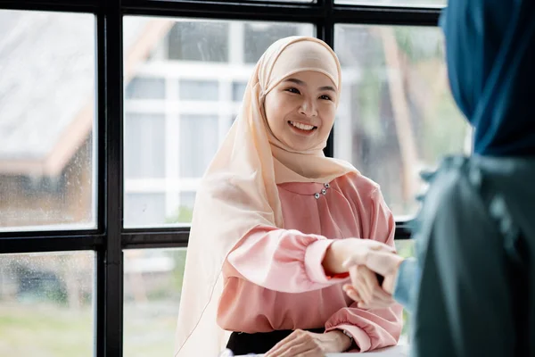 Two hijab Asian women shaking hands after a startup company meeting. run by a young, talented woman. The management concept runs the company of female leaders to grow the company.