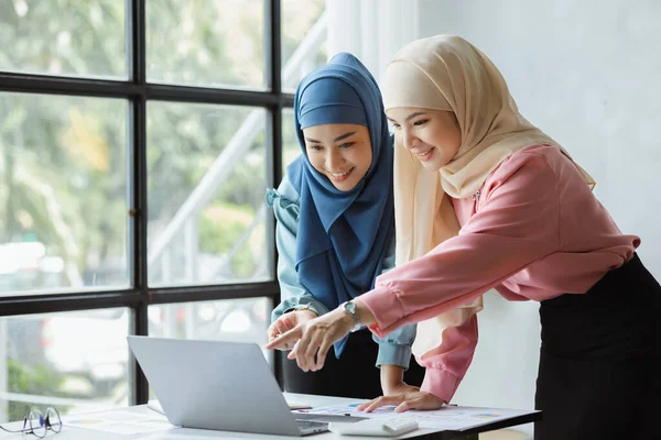 Two hijab-clad Asian women are brainstorming together in a conference room for a startup, run by a young, talented woman. The management concept runs the company of female leaders to grow the company.