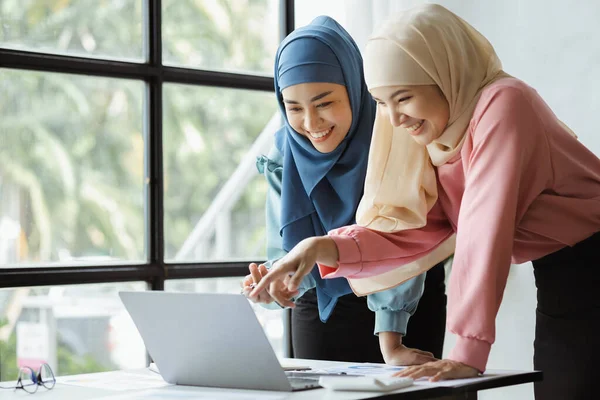Two hijab-clad Asian women are brainstorming together in a conference room for a startup, run by a young, talented woman. The management concept runs the company of female leaders to grow the company.