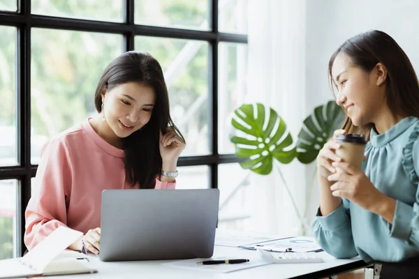 Atmosphere in the office of a startup company, two female employees are discussing, brainstorming ideas to working on summaries and marketing plans to increase sales and prepare reports to managers.