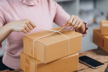 Paketi müşteri kutusuna bağlayan Asyalı bir kadın, çevrimiçi bir mağazası var, özel bir nakliye şirketi aracılığıyla paketleyip gönderiyor. Çevrimiçi satış ve online alışveriş kavramları.