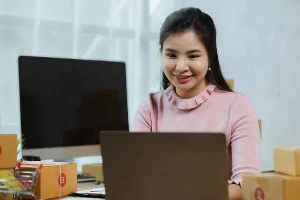 A beautiful Asian business owner opens an online store, she is checking orders from customers, sending goods through a courier company, concept of a woman opening an online business.