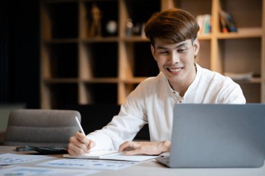 A man sits in the office of a startup company, he is an employee working in the marketing department, planning marketing to grow the company. Concept of working in a startup company office.
