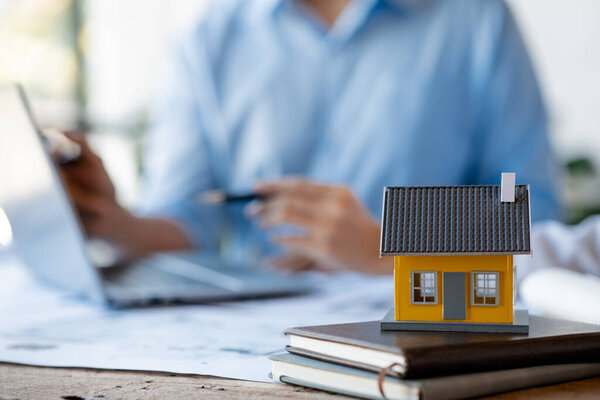 Close-up, a model of a house is placed on a table in the conference room of an architect and engineer meeting to edit a house plan designed for a housing project. Interior design and decoration ideas.