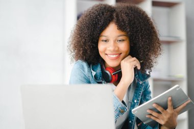 American teenage woman sitting in white office with laptop, she is a student studying online with laptop at home, university student studying online, online web education concept.