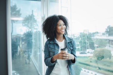 Amerikalı bir kadın, elinde bir fincan sıcak kağıt kahveyle bir şirketin toplantı odasında pencerenin önünde duruyor. Uluslararası bir pazarlama şirketinin çalışanı, bir şirket toplantısına katılıyor..
