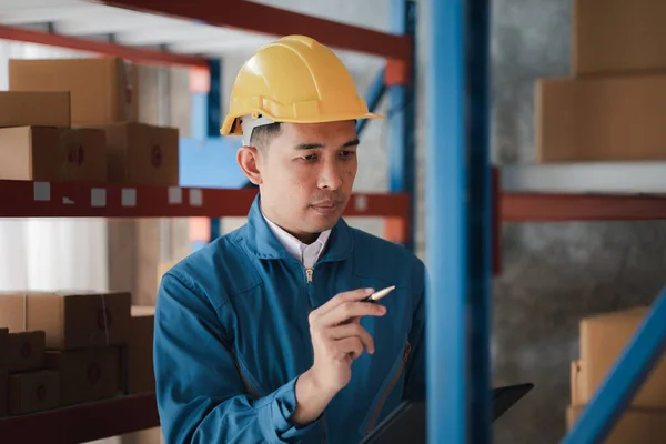 Asian man wearing protective clothing working in a warehouse, he is checking stock, wearing protective clothing while working at a large warehouse according to company policy and worker safety.