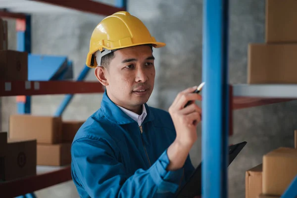 Asian man wearing protective clothing working in a warehouse, he is checking stock, wearing protective clothing while working at a large warehouse according to company policy and worker safety.