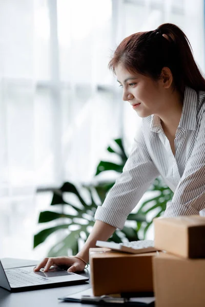 A beautiful Asian business owner opens an online store, she is checking orders from customers, sending goods through a courier company, concept of a woman opening an online business.