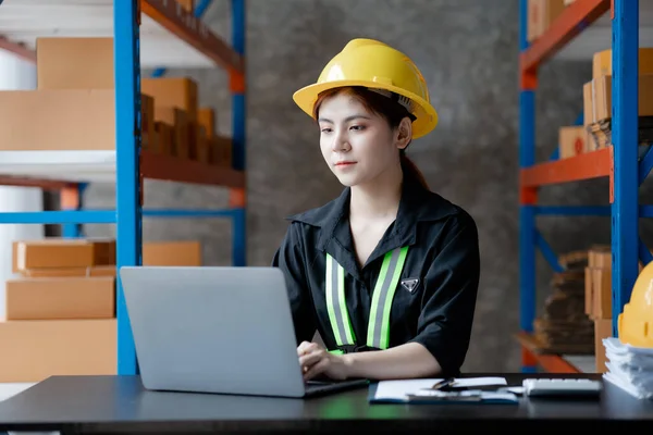 Asian female worker wearing a safety vest is in a warehouse, checking orders and checking balances in a computer system. The concept of working in the warehouse and working in the warehouse is safe.