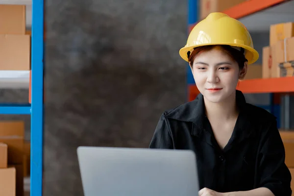 Asian female worker wearing a safety vest is in a warehouse, checking orders and checking balances in a computer system. The concept of working in the warehouse and working in the warehouse is safe.