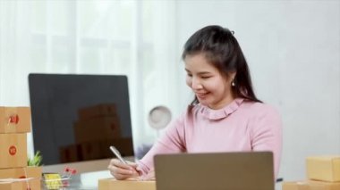Woman who runs an e-commerce business is writing a list of customers on paper before shipping to them, she runs an e-commerce business on websites and social media. Concept of selling products online.
