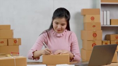 Bir e-ticaret şirketini işleten kadın, onlara göndermeden önce müşterilerin bir listesini kağıda yazıyor. Web sitelerinde ve sosyal medyada bir e-ticaret şirketi işletiyor. Çevrimiçi ürün satma kavramı.