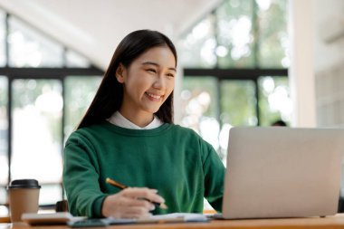 Asian woman working on laptop, female employee of a marketing company, she is working on a marketing plan for a company to generate income and profit, grow sales. Marketing planning concept.