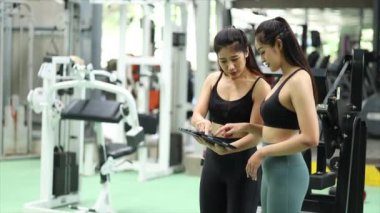 Spor salonunda antrenman yapan iki kadın, bir bayan antrenör ve bir müşteri eğitim programının detaylarını, nasıl forma girip kilo verilebileceğini açıklamak için spor salonunda sohbet ediyorlar. Fitness eğitim konsepti.