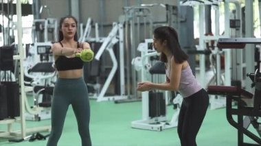 İki kadın spor salonunda antrenman yapıyor, bayan antrenör müşterileri egzersizlerle çalıştırıyor, egzersiz yapmadan önce ısınıyor ve sağlık hizmetleri için fitness merkezine gidiyor. Fitness eğitim konsepti.