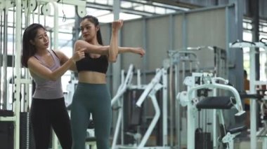 İki kadın spor salonunda antrenman yapıyor, bayan antrenör müşterileri egzersizlerle çalıştırıyor, egzersiz yapmadan önce ısınıyor ve sağlık hizmetleri için fitness merkezine gidiyor. Fitness eğitim konsepti.