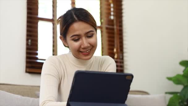 自宅のリビングルームでソファでタブレットをしている女性は 一日の仕事の後の週末にリラックスしていて オンラインで買い物をしてクレジットカードで支払いをしています クレジットカード決済の概念 — ストック動画