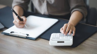 Bir şirketin mali belgelerindeki rakamları hesaplamak için hesap makinesi kullanan bir işadamı, şirketin nasıl büyüyeceğini planlamak için tarihsel finansal verileri analiz ediyor. Mali konsept.