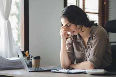 Beautiful Asian woman working in an office, she is a businesswoman who owns a company, she has a headache due to long and large paperwork leaving her tired and dizzy. The concept of sickness from work