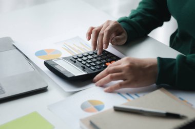 Bir şirketin mali belgelerindeki rakamları hesaplamak için hesap makinesi kullanan bir iş kadını, şirketin nasıl büyüyeceğini planlamak için tarihsel finansal verileri analiz ediyor. Mali konsept.