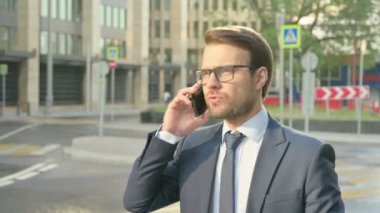 İş adamı sokakta yürürken telefonda konuşuyor.