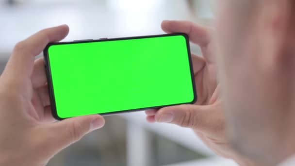 Man op zoek naar smartphone met groene chroma scherm, close-up — Stockvideo