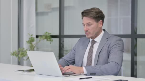 Hombre de mediana edad sacudiendo la cabeza como ninguna señal mientras se utiliza el ordenador portátil en la oficina — Vídeo de stock