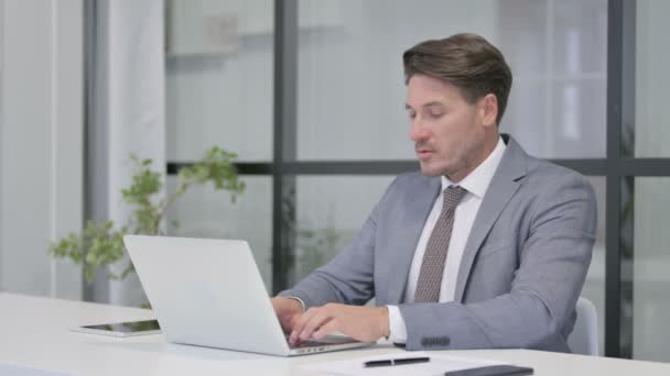 Uomo di mezza età che festeggia mentre utilizza il computer portatile in ufficio sul banco — Video Stock