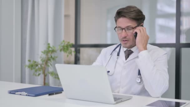 Doktorn pratar i telefon medan du arbetar på laptop — Stockvideo