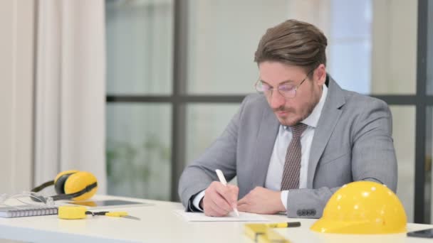 Medelålders ingenjör Skriva på papper i Office — Stockvideo