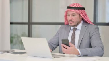 Ofiste dizüstü bilgisayar kullanırken Smartphone kullanan Orta Çağ Arap İşadamı 