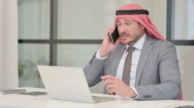 Öfkeli Orta Çağ Arap İşadamı Laptop kullanırken telefonda konuşuyor