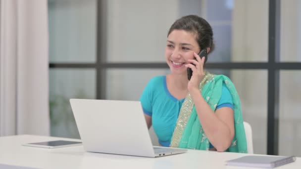 Індійська жінка розмовляє по телефону, користуючись ноутбуком в офісі — стокове відео