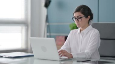 Ofiste dizüstü bilgisayar kullanırken kameraya gülümseyen Hintli İş kadını