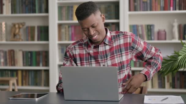 Hombre africano que tiene dolor de espalda mientras usa el ordenador portátil en la oficina — Vídeos de Stock