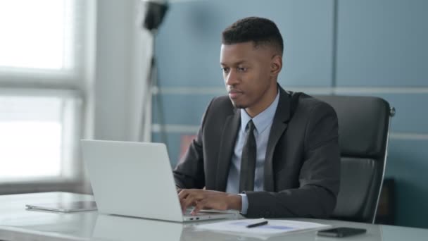 Африканский бизнесмен качает головой без каких-либо признаков при использовании ноутбука в офисе — стоковое видео