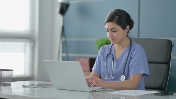 Médico femenino indio sonriendo en la cámara mientras usa el ordenador portátil en la oficina — Vídeos de Stock