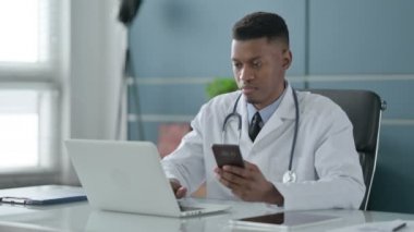 Ofiste dizüstü bilgisayar kullanırken akıllı telefon kullanan Afrikalı Doktor 
