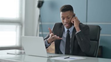 Ofiste dizüstü bilgisayar kullanırken telefonda konuşan kızgın Afrikalı İşadamı