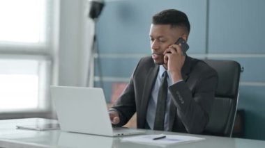 Ofiste dizüstü bilgisayar kullanan Afrikalı İşadamı Smartphone ile konuşuyor